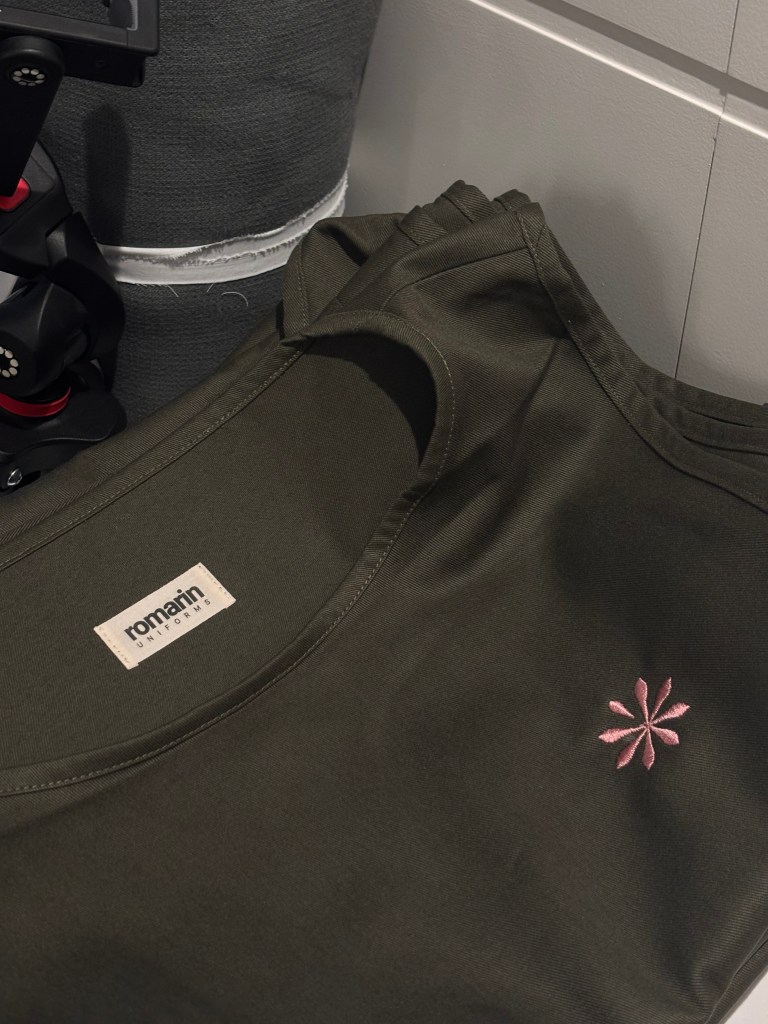Detail of a professional uniform top with embroidered logo, minimalist hospitality workwear for Terres du Val
