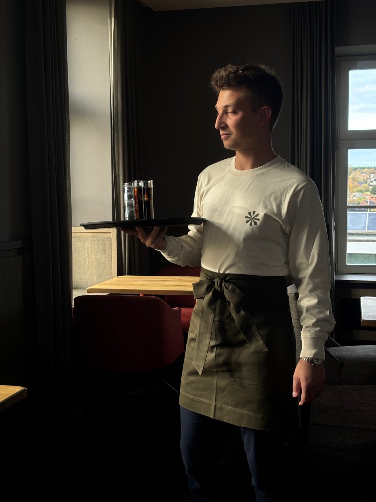 Hospitality staff wearing a professional uniform apron while serving drinks at Terres du Val, minimalist restaurant workwear